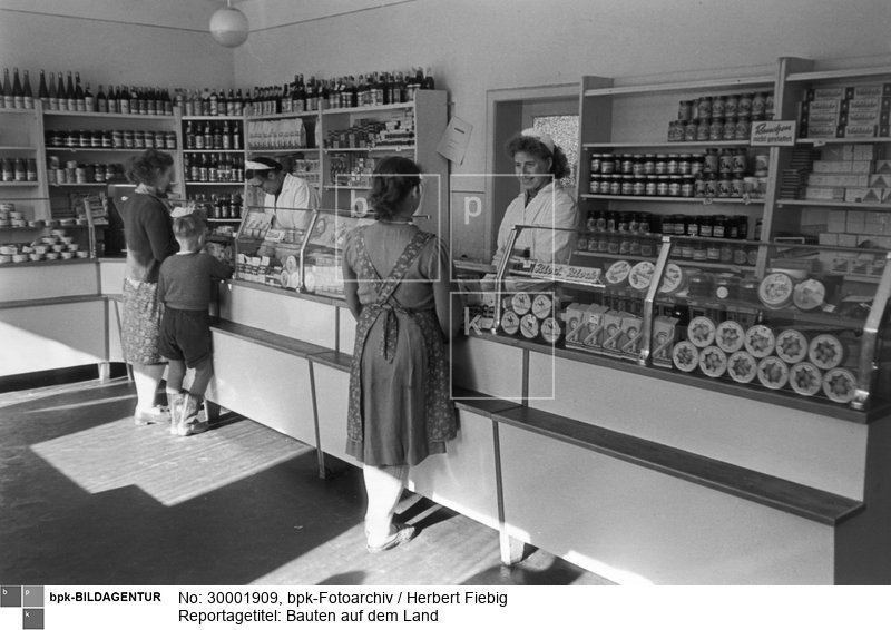 vgl. Bauzeitung 10/1959, S. 231 ("Der Stadt auf dem Lande nachgespürt"): "'Es ist gar kein Vergleich mit den Einkaufsmöglichkeiten, die wir früher hatten', sagte Frau Behm (vorn). Sie ist sehr froh, daß mit diesem Landkaufhaus in Züsenow [=Züsedom!] das Warenangebot reichlicher geworden ist, und der Verkäuferin Ingelore Emmerich macht es ebenfalls Freude, die Wünsche ihrer Kundinnen zu erfüllen"<BR>Aufnahmedatum: April 1959<BR>Material/Technik: Foto<BR>Aufnahmeort: Züsenow, Bezirk Neubrandenburg, DDR<BR>Inventar-Nr.: Fg 0560/01-19<BR>