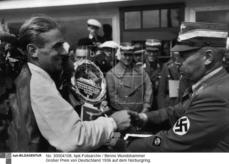 Fotograf: Benno Wundshammer <BR> Der Sieger Bernd Rosemeyer (Auto Union) mit dem Siegerpokal, NSKK-Führer Hühnlein gratuliert <BR> Aufnahmedatum: 26.07.1936 <BR> Aufnahmeort: Nürburgring <BR> Inventar-Nr.: Wu S38/154-26 <BR> Systematik:  <BR> Geschichte / Deutschland / 20. Jh. / NS-Zeit / Sport / Motorsport / allgemein