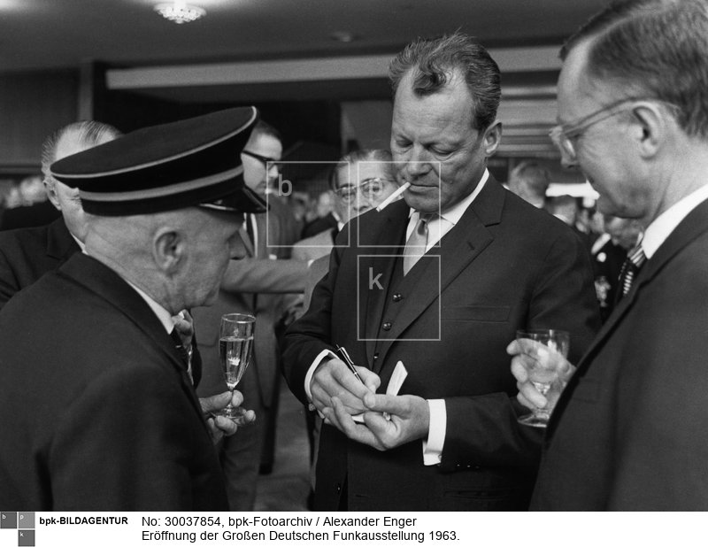 Fotograf: Alexander Enger <BR> Der Regierenden Bürgermeister von Berlin, Willy Brandt (Mitte), gibt auf dem Empfang ein Autogramm. Rechts: Karl Schiller <BR> Aufnahmedatum: 30.08.1963 <BR> Aufnahmeort: Berlin (West) <BR> Inventar-Nr.: Eg 63/9/2-22 <BR> Systematik:  <BR> Geschichte / Deutschland / 20. Jh. / West-Berlin 1949-1990 / Wirtschaft / Industrie / Elektrotechnische Industrie / Messen, Ausstellungen / Internationale Funkausstellung