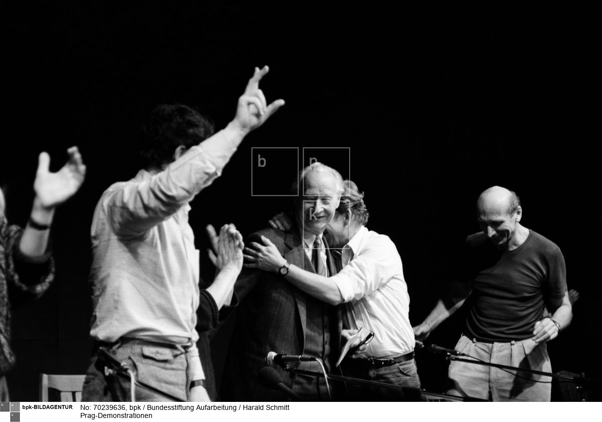 Alexander Dubcek (l.), Leitfigur des Prager Frühlings 1968, und Vaclav Havel, Schriftsteller und prominentester Regimegegner, auf dem Podium des Bürgerforums am 24. November. Aus dem Publikum wird ihnen zugerufen, dass der Prager Vorsitzende der Kommunistischen Partei zurückgetreten ist. Dubcek und Havel springen auf und umarmen sich. Sie wissen: Das Regime ist am Ende, das ist ihr Sieg. <BR>Aufnahmedatum: 24.11.1989<BR>Material/Technik: Foto<BR>Aufnahmeort: Prag / Tschechoslowakei (Tschechien)<BR>Inventar-Nr.: HSchmitt17_neu