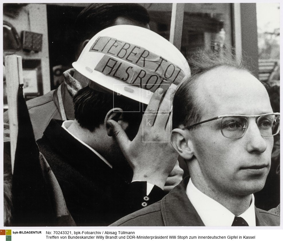 Demonstranten am Bahnhof. Einer von ihnen trägt einen Helm mit der Parole "Lieber tot als rot"
<BR>Aufnahmedatum: 21.05.1970<BR>Material/Technik: Foto / Silbergelatine auf Barytpapier<BR>Bildformat (Foto): 23,5 x 29,3 cm<BR>Aufnahmeort: Kassel / Deutschland<BR>Inventar-Nr.: Tü 70/161-28<BR>