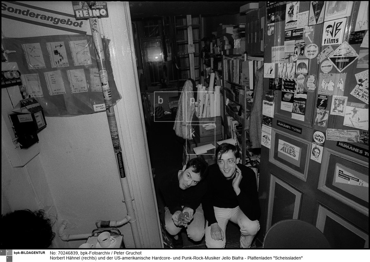 1980 eröffnete Hähnel seinen Plattenladen Scheissladen in Berlin-Kreuzberg. Er gehörte mit wenigen anderen Läden zu den Vertriebsorten einer Untergrund-Musik von Punk, experimenteller Musik bis zur Neuen Deutschen Welle.<BR>Person: Norbert Hähnel (1951-), deutscher Sänger aus Berlin-Kreuzberg. Er war der Inhaber des Plattenladens Scheissladen. Außerdem war er eine Zeit als Veranstalter von Punk-Konzerten tätig.

Jello Biafra (bürgerlich Eric Reed Boucher (1958-), US-amerikanischer Hardcore- und Punk-Rock-Musiker sowie politischer Aktivist, der als Leadsänger der Punk-Band Dead Kennedys Bekanntheit erlangte.<BR>Aufnahmedatum: 10.12.1982<BR>Material/Technik: Foto<BR>Aufnahmeort: Berlin-Kreuzberg (Berlin West)<BR>