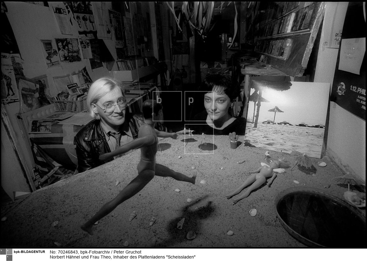 1980 eröffnete Hähnel seinen Plattenladen Scheissladen in Berlin-Kreuzberg. Er gehörte mit wenigen anderen Läden zu den Vertriebsorten einer Untergrund-Musik von Punk, experimenteller Musik bis zur Neuen Deutschen Welle. 1987 schloss Hähnel den Scheissladen und eröffnete eine Kneipe namens Enzian, die er bis 2007 betrieb.<BR>Person: Norbert Hähnel (1951-), deutscher Sänger aus Berlin-Kreuzberg. Er war der Inhaber des Plattenladens Scheissladen. Außerdem war er eine Zeit als Veranstalter von Punk-Konzerten tätig.<BR>Aufnahmedatum: November 1983<BR>Material/Technik: Foto<BR>Aufnahmeort: Berlin-Kreuzberg (Berlin West)<BR>