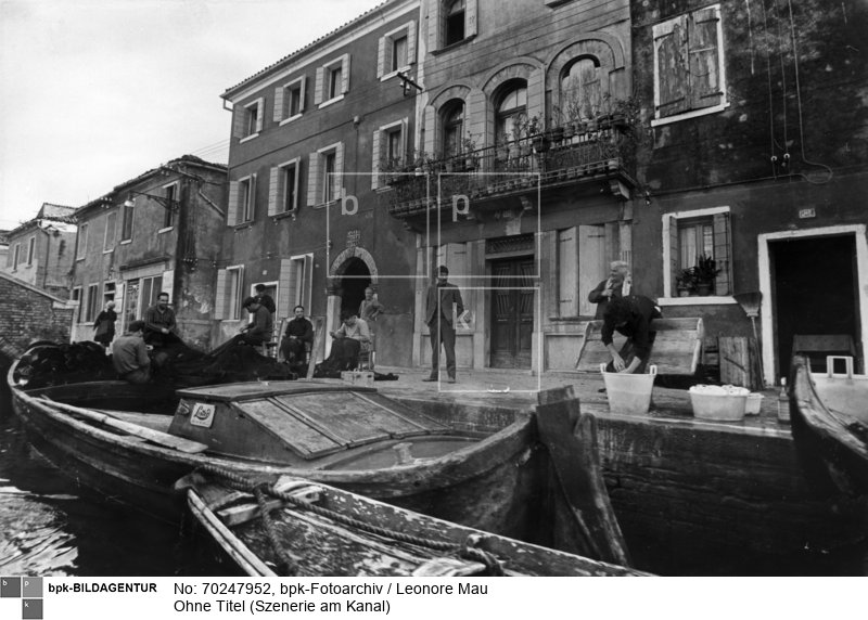 Szenerie am Kanal in Venedig. Eine Gruppe von Männern sitzt auf der Straße und dem angelegten Boot und flickt ein Fischernetz. Daneben wäscht eine Person Geschirr in großen Schüsseln. Sie wird von der Männergruppe und anderen Leuten auf der Straße beobachtet.<BR>Aufnahmedatum: 1959 - 1961<BR>Material/Technik: Foto / Silbergelatine auf Barytpapier<BR>Bildformat (Foto): 16,0 x 23,9 cm<BR>Aufnahmeort: Venedig<BR>Inventar-Nr.: LM-506601<BR>