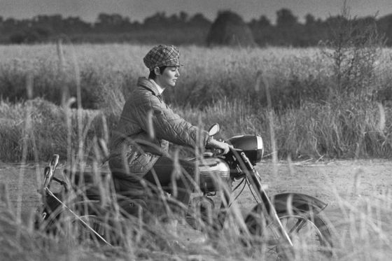 Eine junge Frau fährt mit dem Motorrad an Kornfeldern vorbei