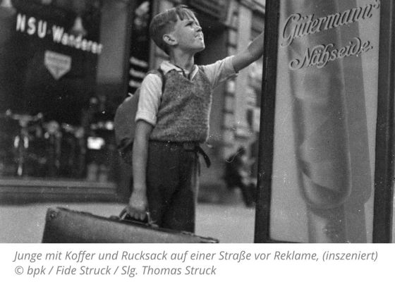 Junge mit Koffer und Rucksack auf einer Straße vor Reklame, (inszeniert)